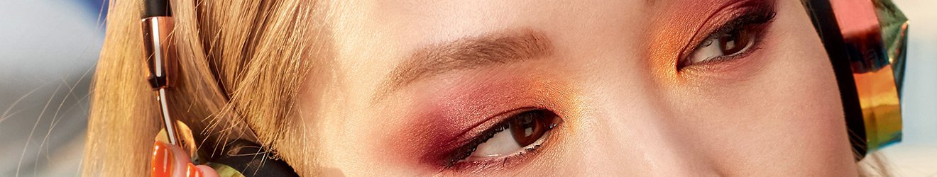 ภาพแบนเนอร์ประกอบผลิตภัณฑ์อายแชโดว์ของเมย์เบลลีน - ภาพระยะใกล้ของผู้หญิงชาวเอเชียผมบลอนด์สวมหูฟัง ทาอายแชโดว์สีสีนสดใส